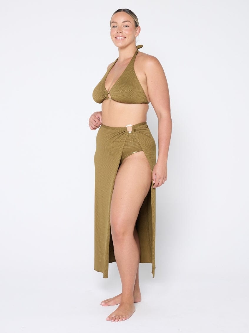 Woman wearing an olive green bikini and matching sarong on a white background