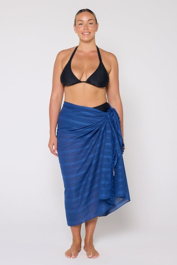 Woman wearing a black bikini top and blue striped sarong on a white background