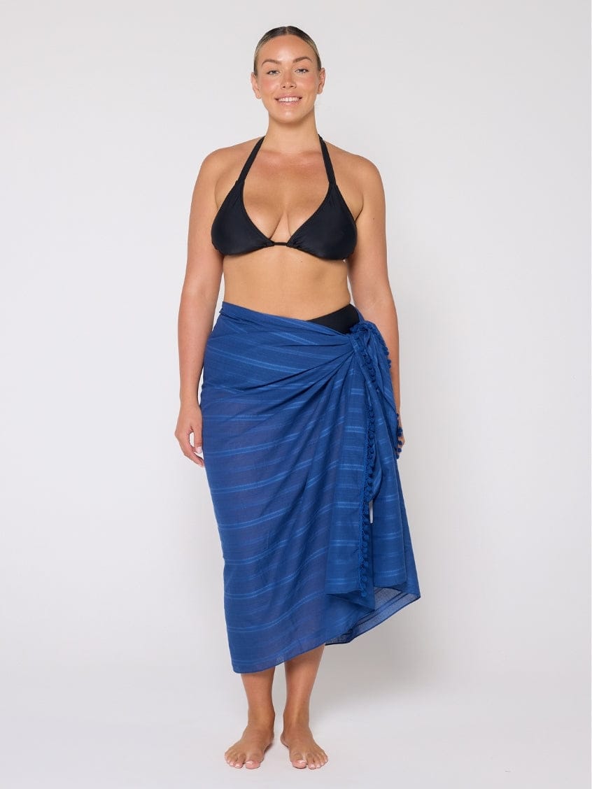 Woman wearing a black bikini top and blue striped sarong on a white background