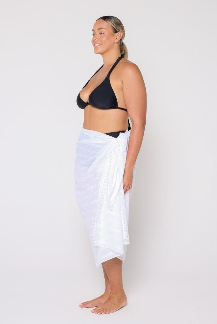 Woman wearing a black bikini top and white sarong on a plain background
