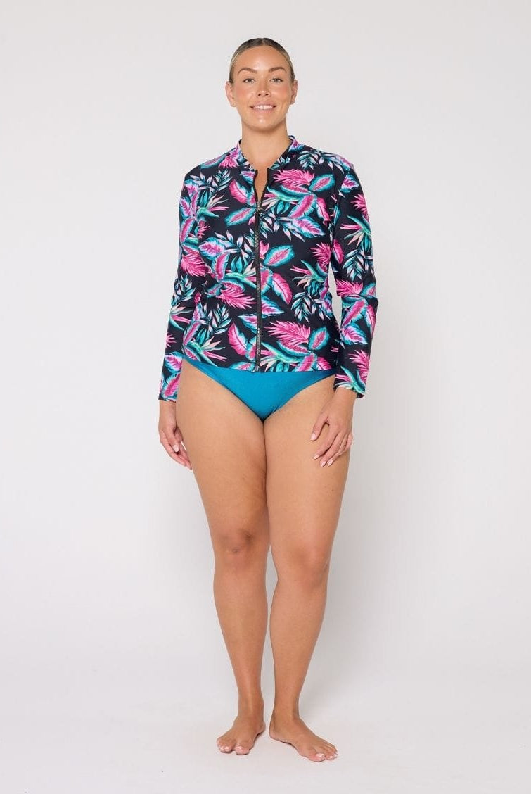 Woman wearing a colorful long-sleeve rash guard and blue swimsuit on a white background