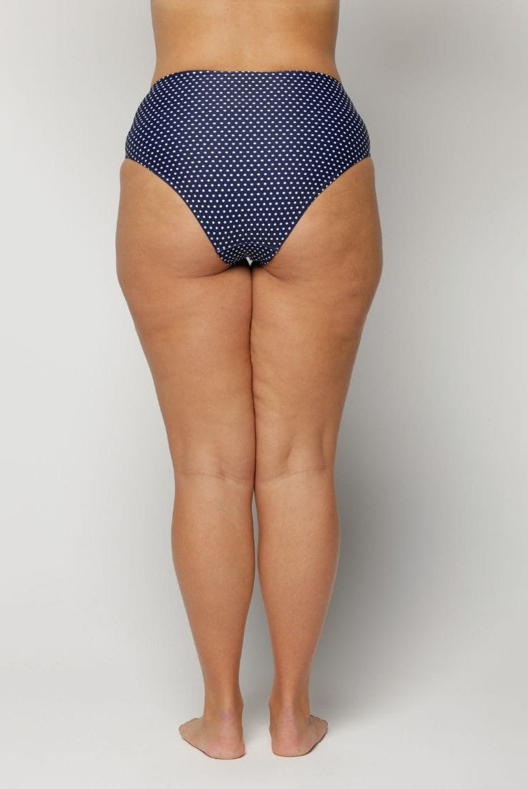 Woman wearing a blue polka dot bikini bottom on a plain background