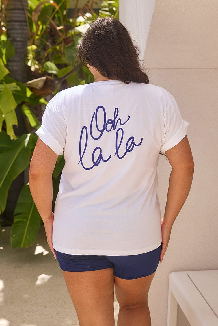 Person wearing a white t-shirt with 'Ooh la la' text in blue on the back, standing outdoors.