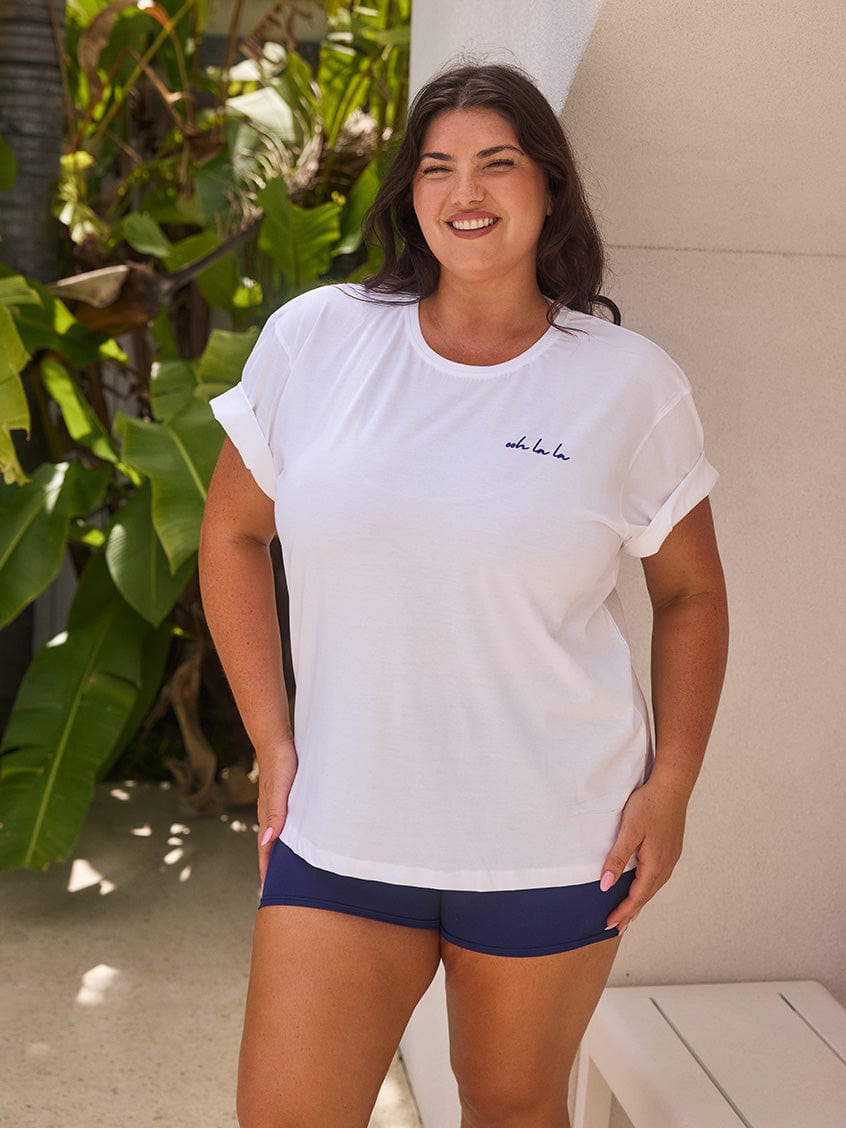 Woman wearing a white t-shirt and navy shorts standing outdoors with plants in the background