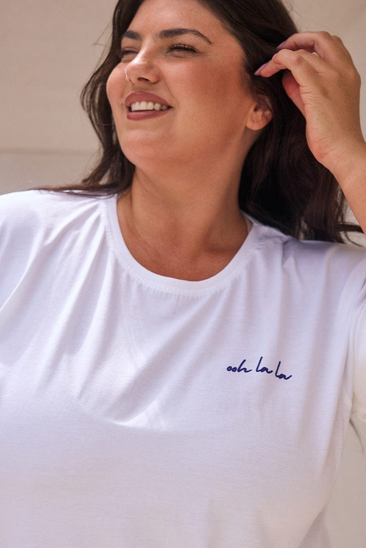 Woman wearing a white t-shirt with a logo, smiling outdoors.