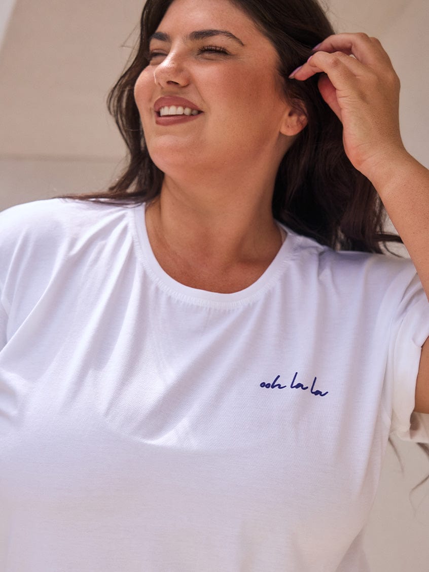 Woman wearing a white t-shirt with a logo, smiling outdoors.