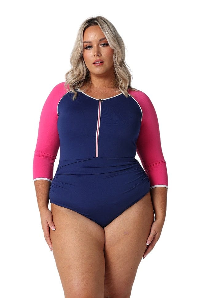 Blonde model in studio wearing chlorine resistant navy and pink one piece with elbow length sleeves