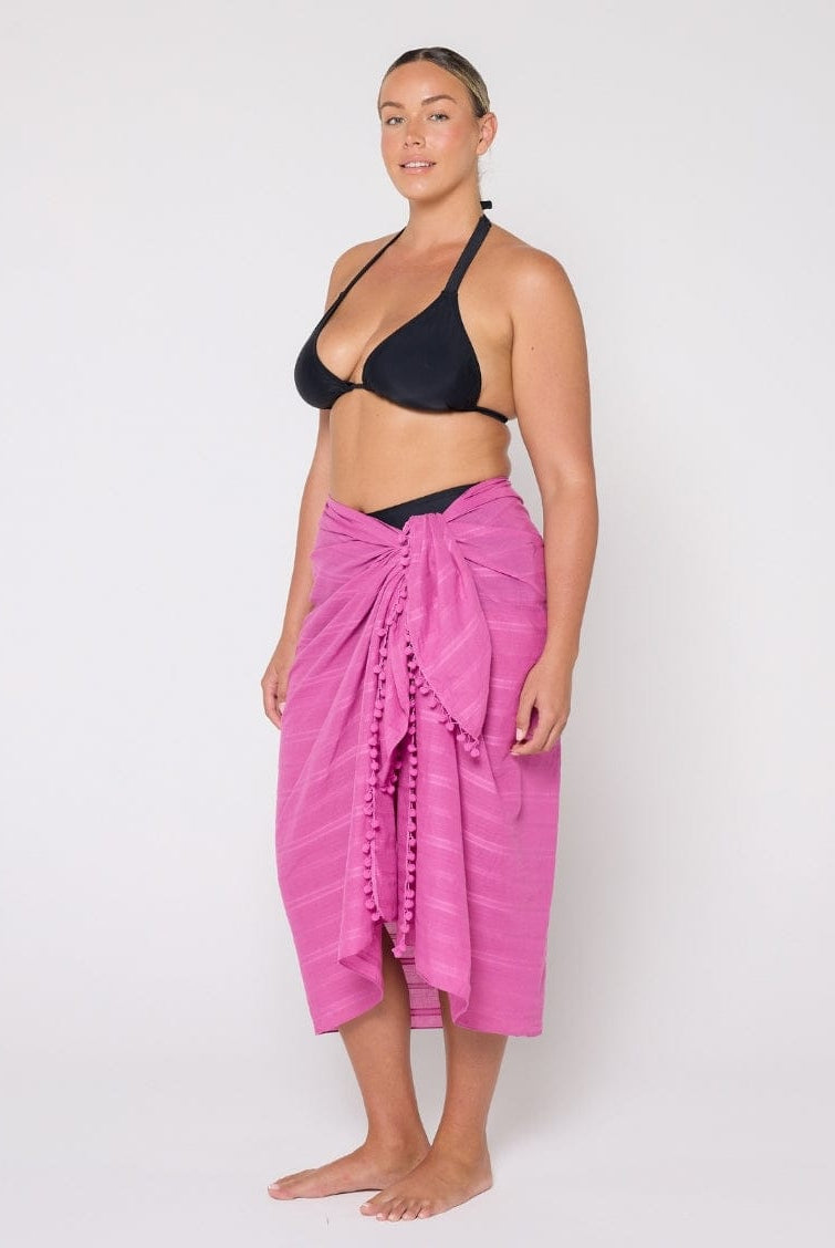 Woman wearing a black bikini top and pink sarong on a white background