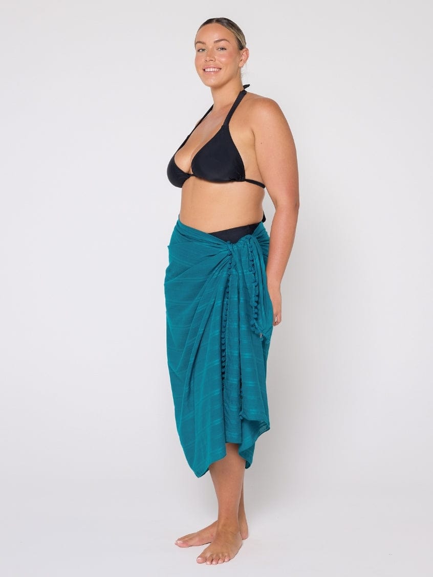 Woman wearing a black bikini and teal sarong on a white background