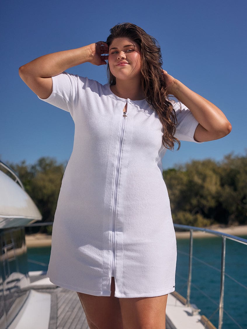 Woman in a white dress standing on a boat with a clear blue sky and trees in the background