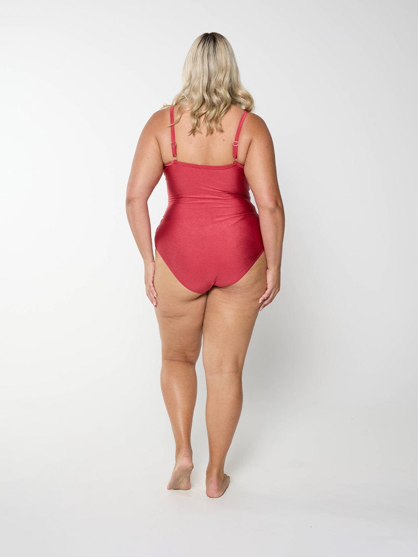 Blonde curve woman in studio wearing a deep red metallic one piece with adjustable straps
