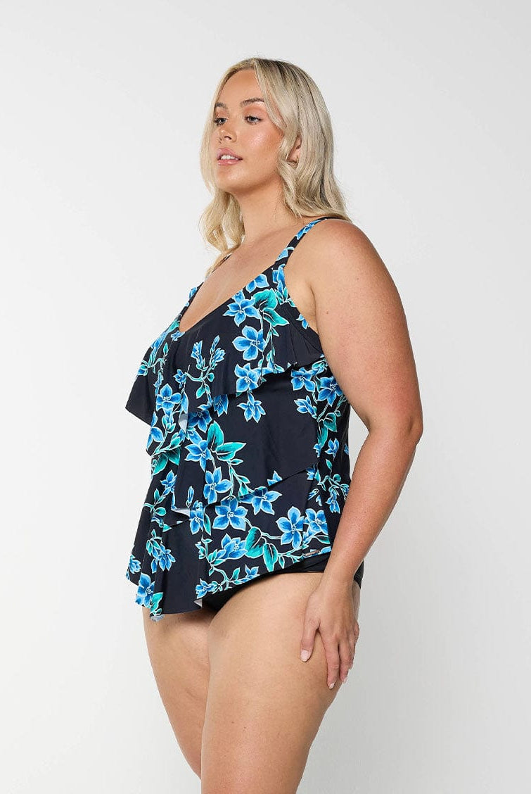 Blonde model shows side of tankini top with blue flowers and figure flattering ruffles
