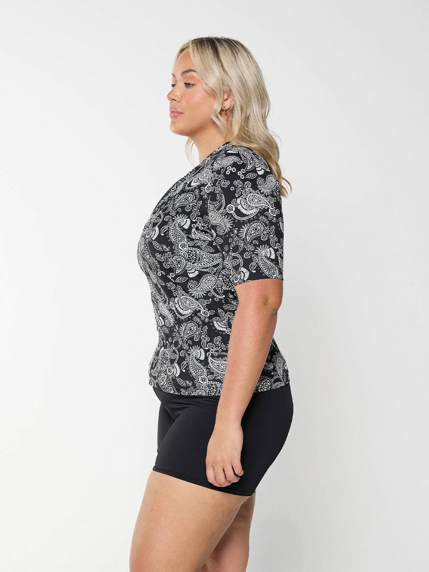 Side profile of blonde curve model in studio wearing short sleeve rash vest in chlorine resistant in paisley print