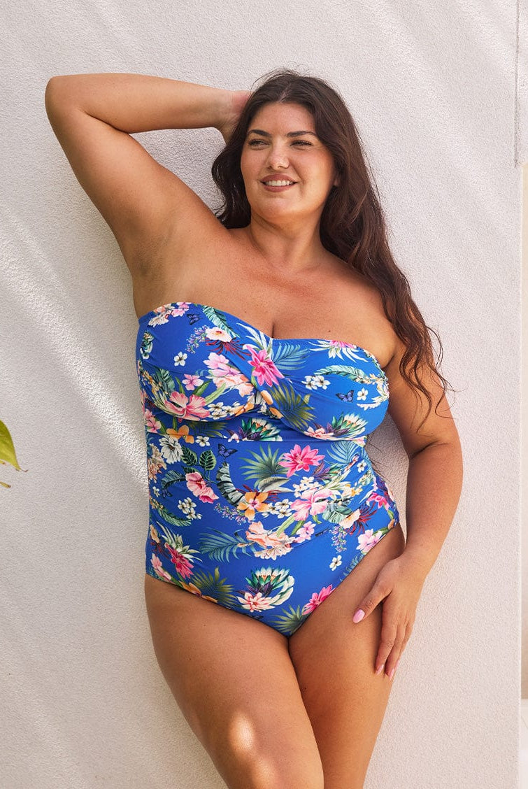 Brunette model wears flattering bandeau one piece in blue floral print with removable straps