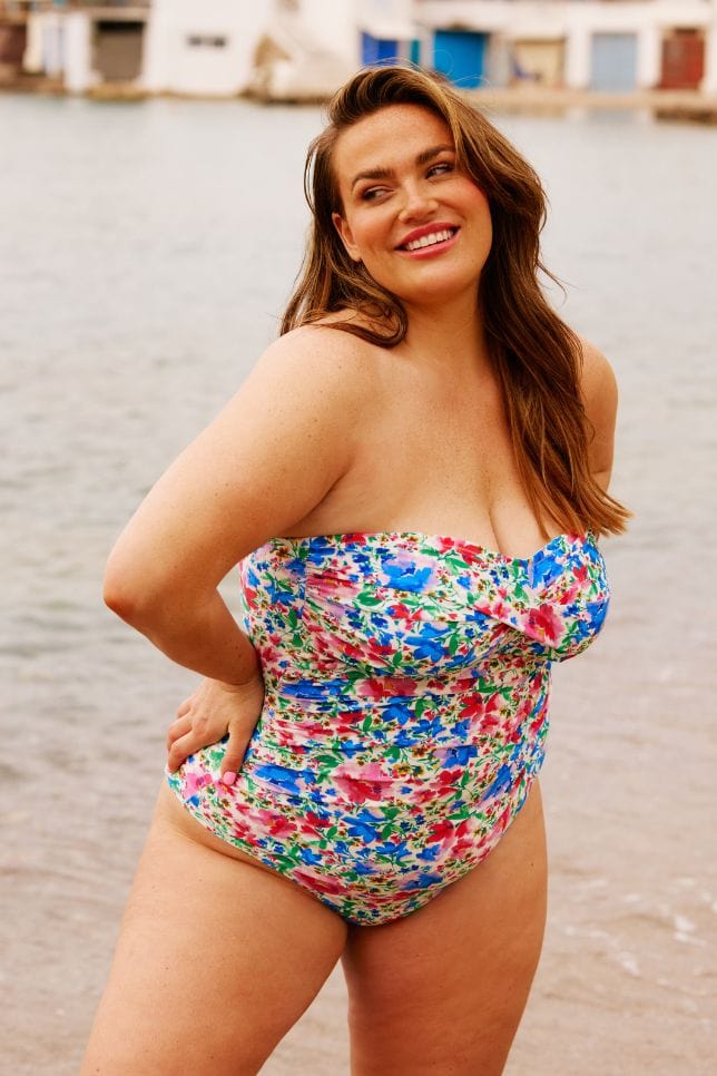 Brunette plus size model on beach wearing a flattering bandeau one piece with removable straps in bright colours