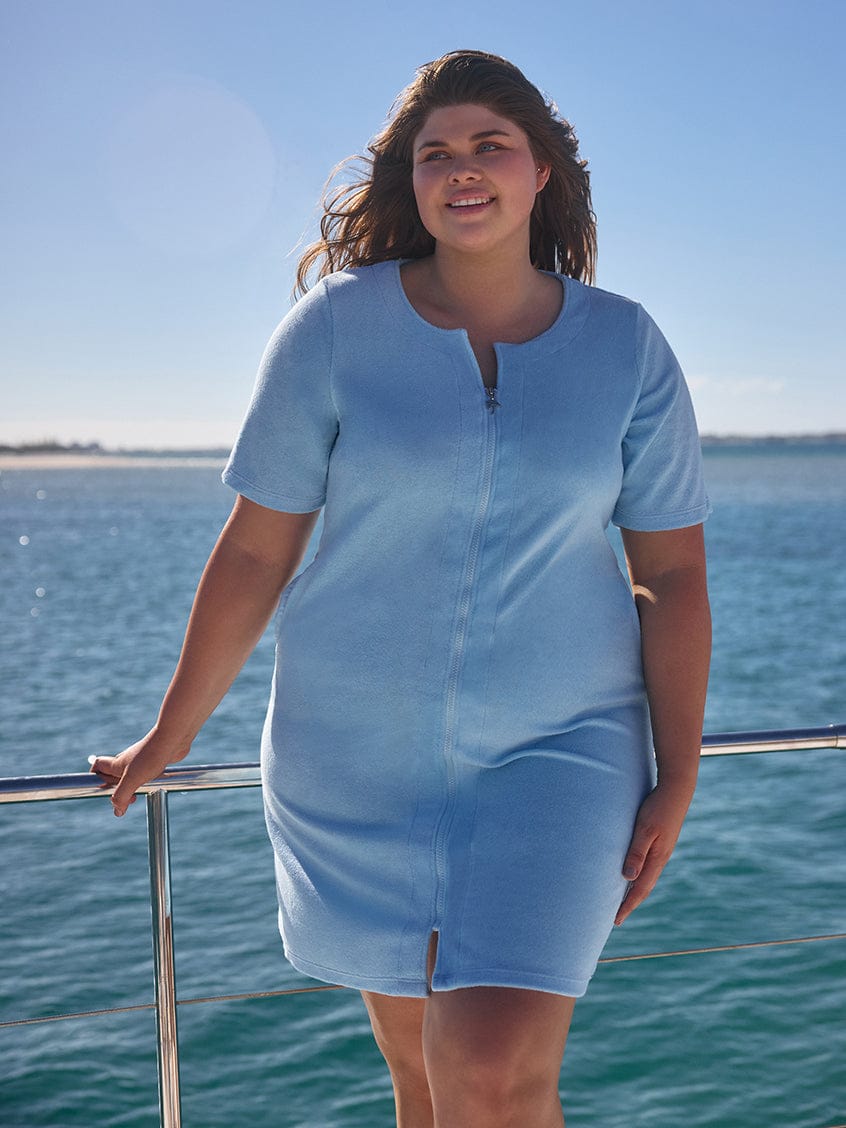 Woman wearing a light blue dress standing on a boat with water and sky in the background