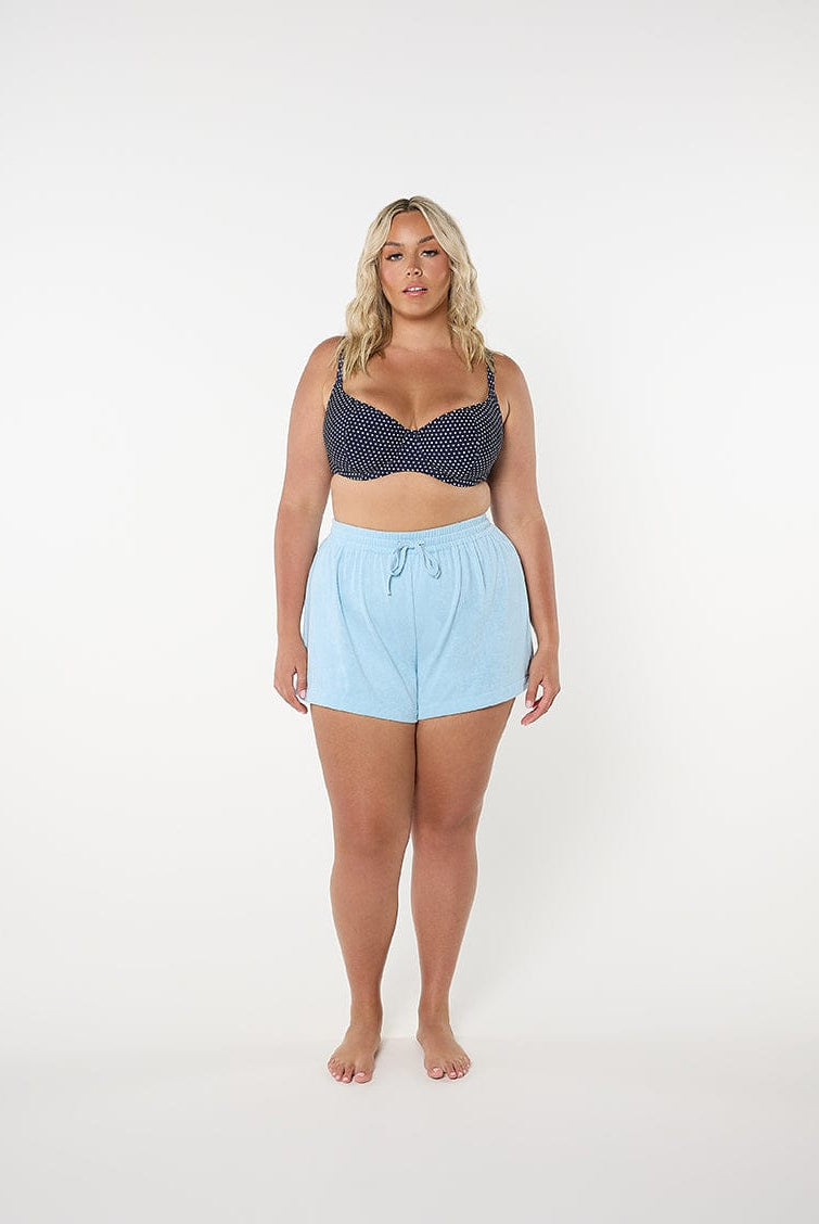 Woman wearing a navy patterned top and light blue shorts on a white background