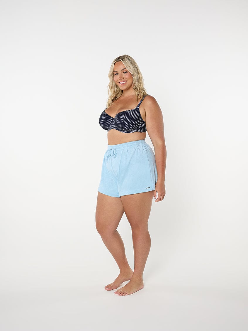 Woman wearing a navy polka dot bikini top and light blue shorts on a white background