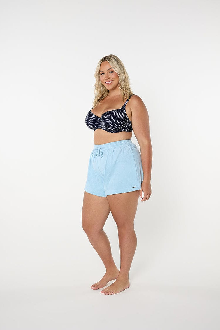 Woman wearing a navy polka dot bikini top and light blue shorts on a white background