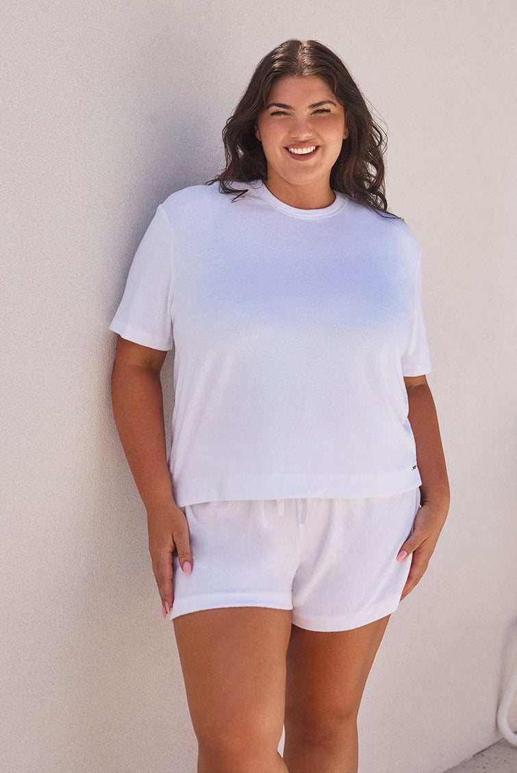 Woman wearing a white t-shirt and shorts against a light-colored wall.