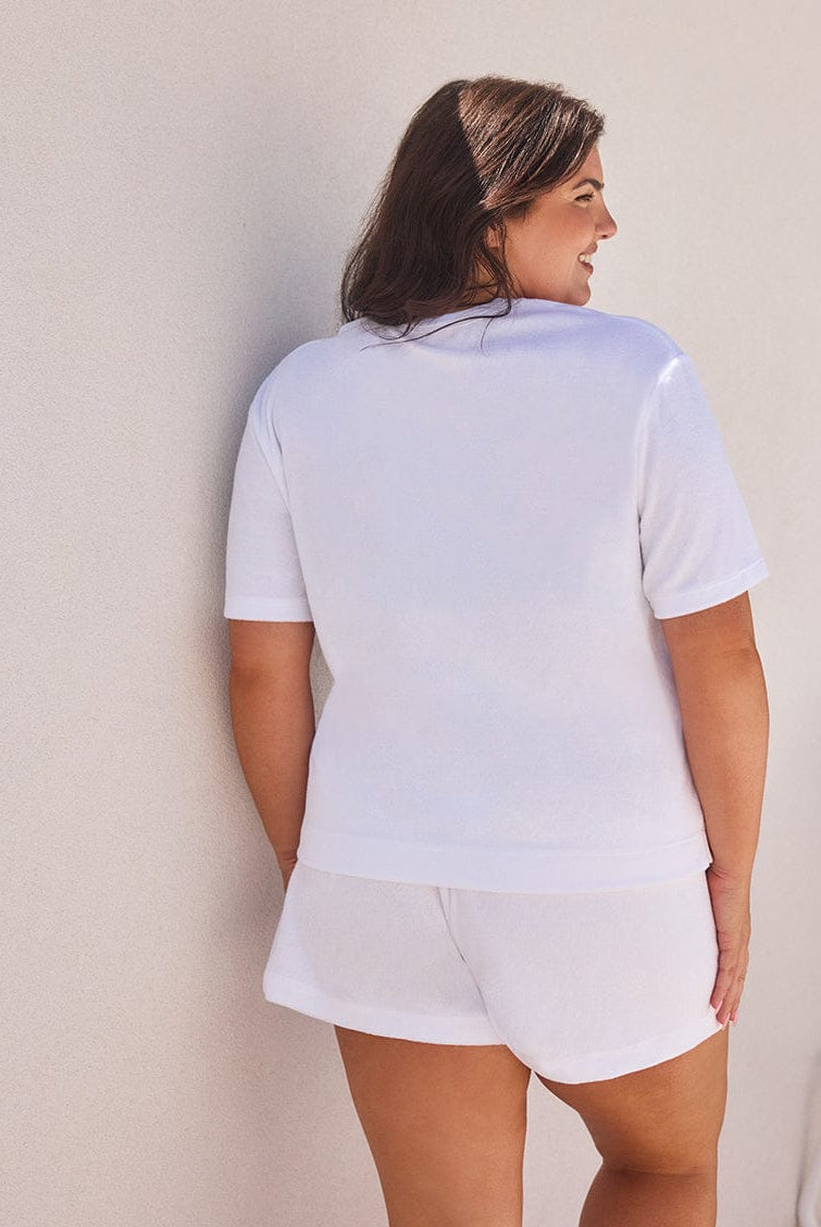 Woman wearing a light blue t-shirt and white shorts against a neutral wall.