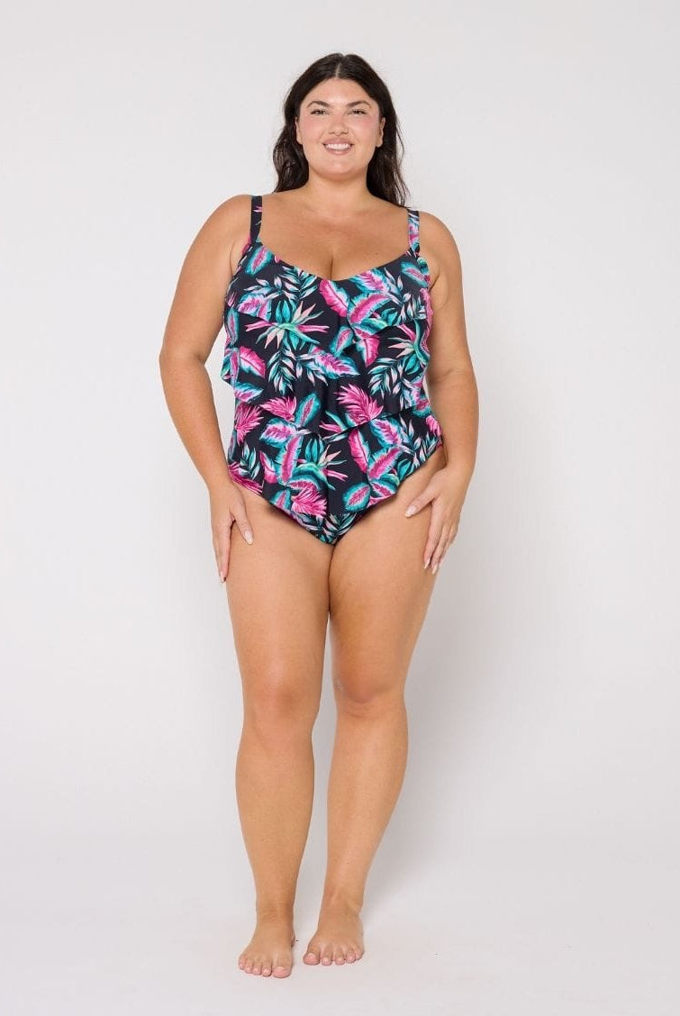 Woman wearing a tiered design tropical leaf patterned swimsuit on a white background
