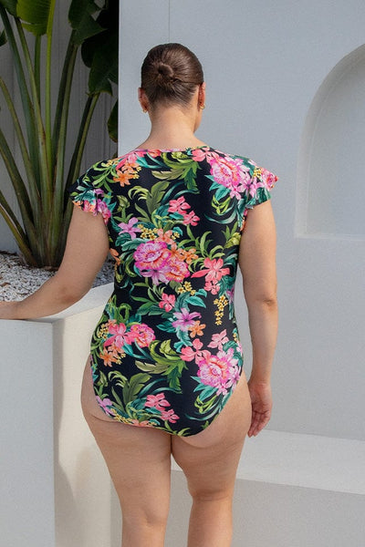 Woman in plus size floral print one piece with ruffle sleeves and high neck zip front