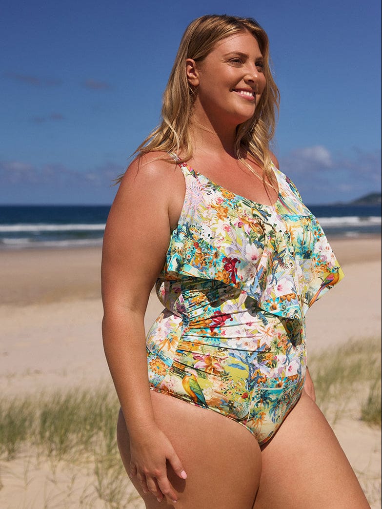 Woman in a floral swimsuit standing on a beach with ocean and sky in the background