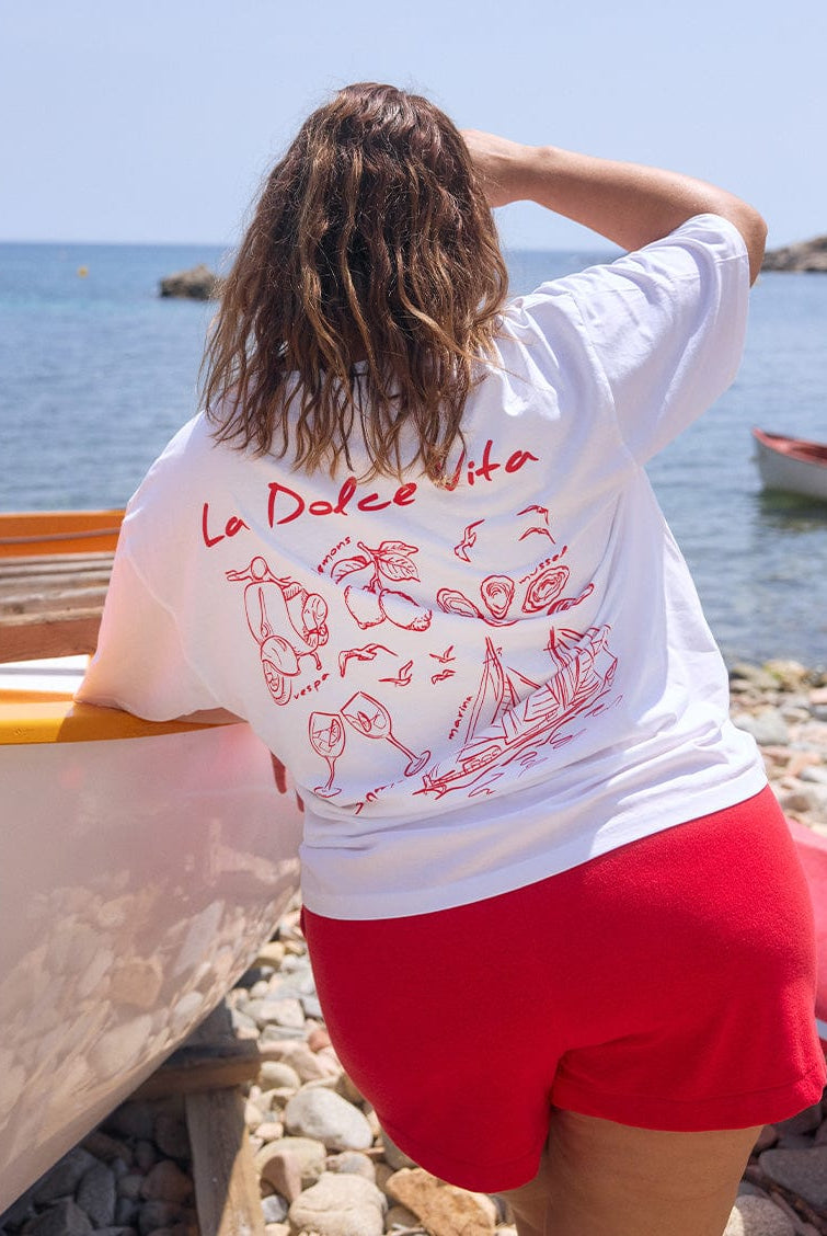 Back of model on beach wearing short sleeve t shirt top with red illustrations on the back