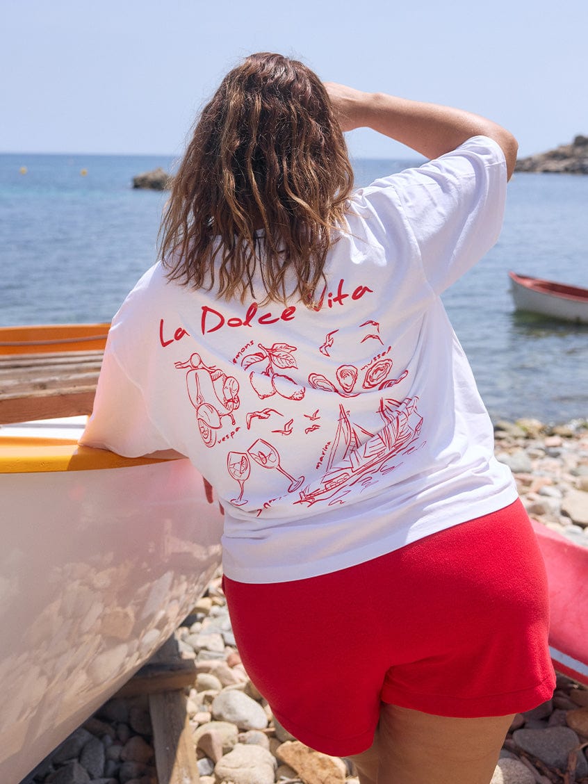Back of model on beach wearing short sleeve t shirt top with red illustrations on the back