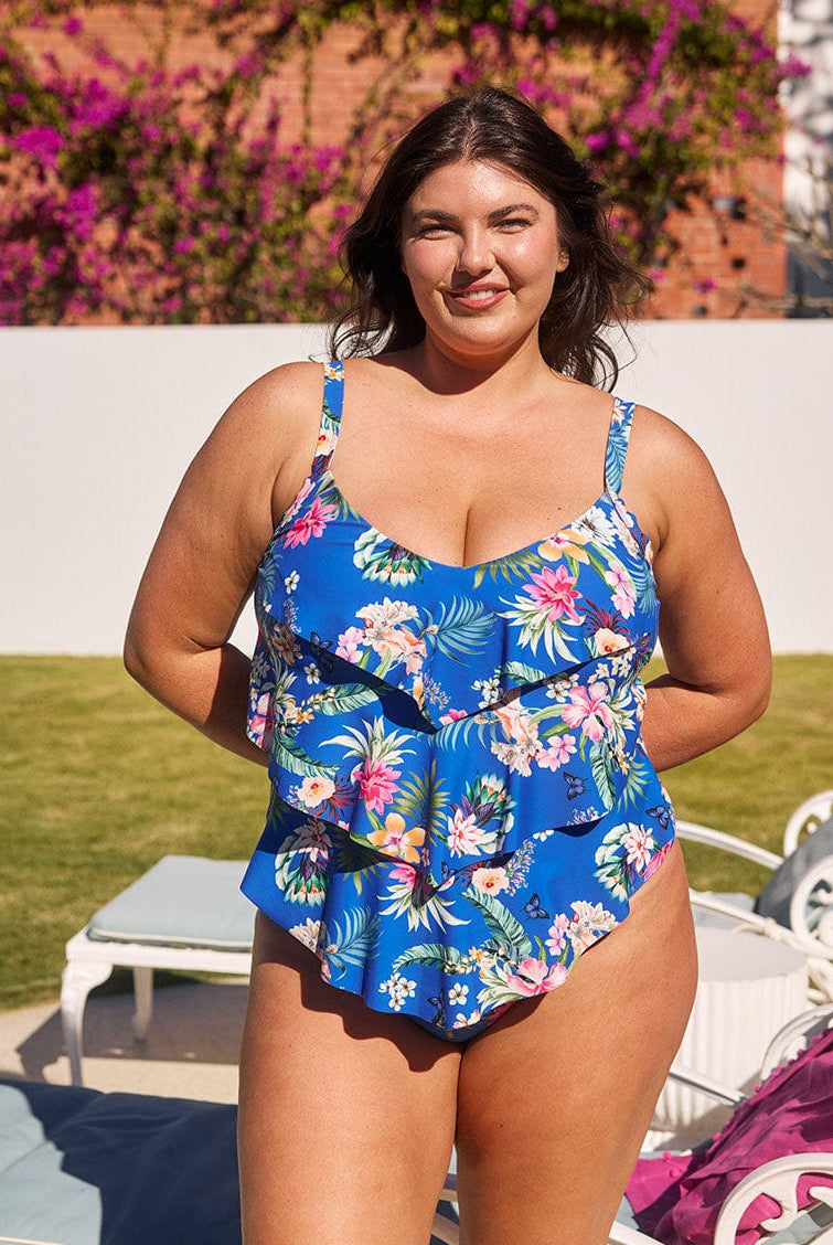 Brunette model wears flattering blue floral one piece with 3 tiers for tummy control