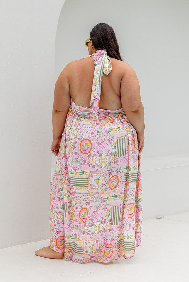 Plus size model wearing halter maxi dress with tie detail and slit down side in bright coloured fruit print