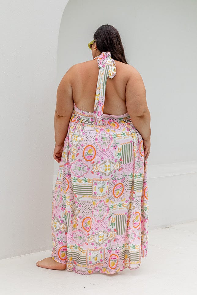 Plus size model wearing halter maxi dress with tie detail and slit down side in bright coloured fruit print