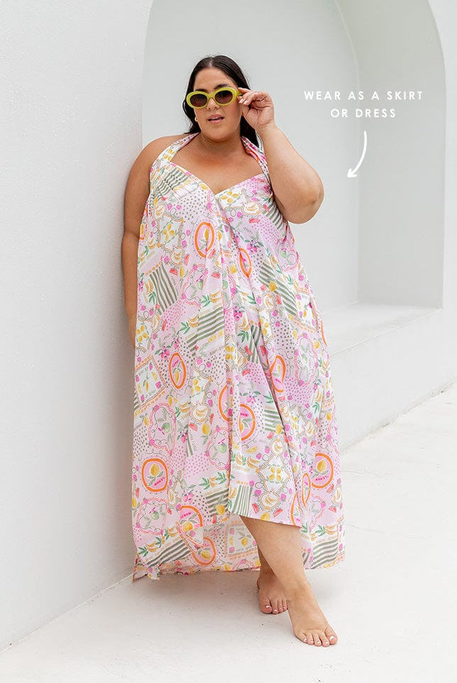 Brunette model wearing skirt worn as maxi halter dress with multi coloured fruit print on pink base Australia