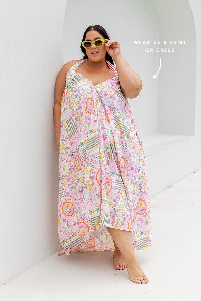 Brunette model wearing skirt worn as maxi halter dress with multi coloured fruit print on pink base Australia