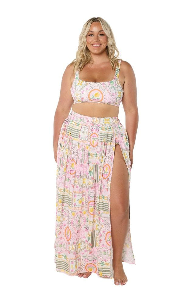 Blonde model in studio wearing high waisted maxi skirt with slit and pleating detail in bright fruit print