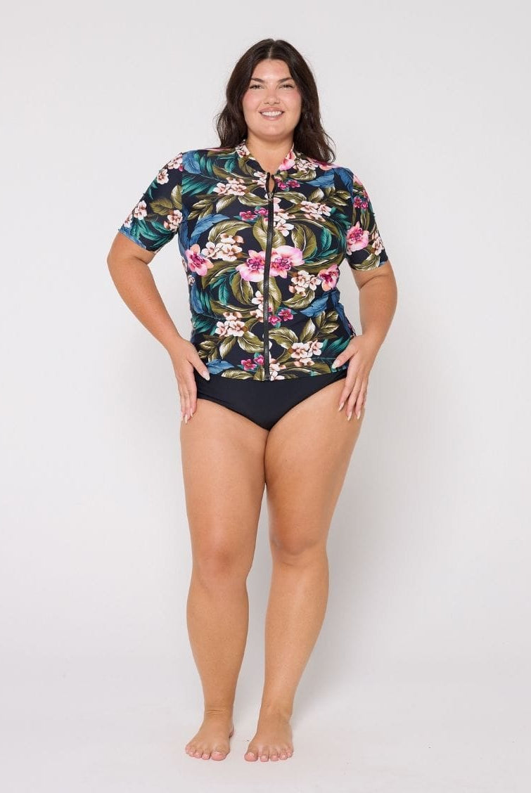 Woman wearing a floral rash guard and black swimsuit bottoms on a white background