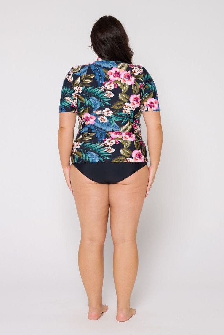 Person wearing a floral and leaf patterned rash top with a plain background