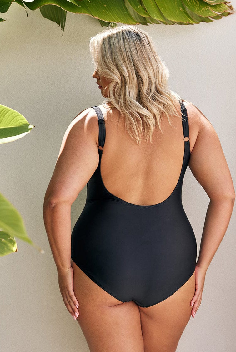 back of women wearing a black one piece swimsuit standing in front of a white wall