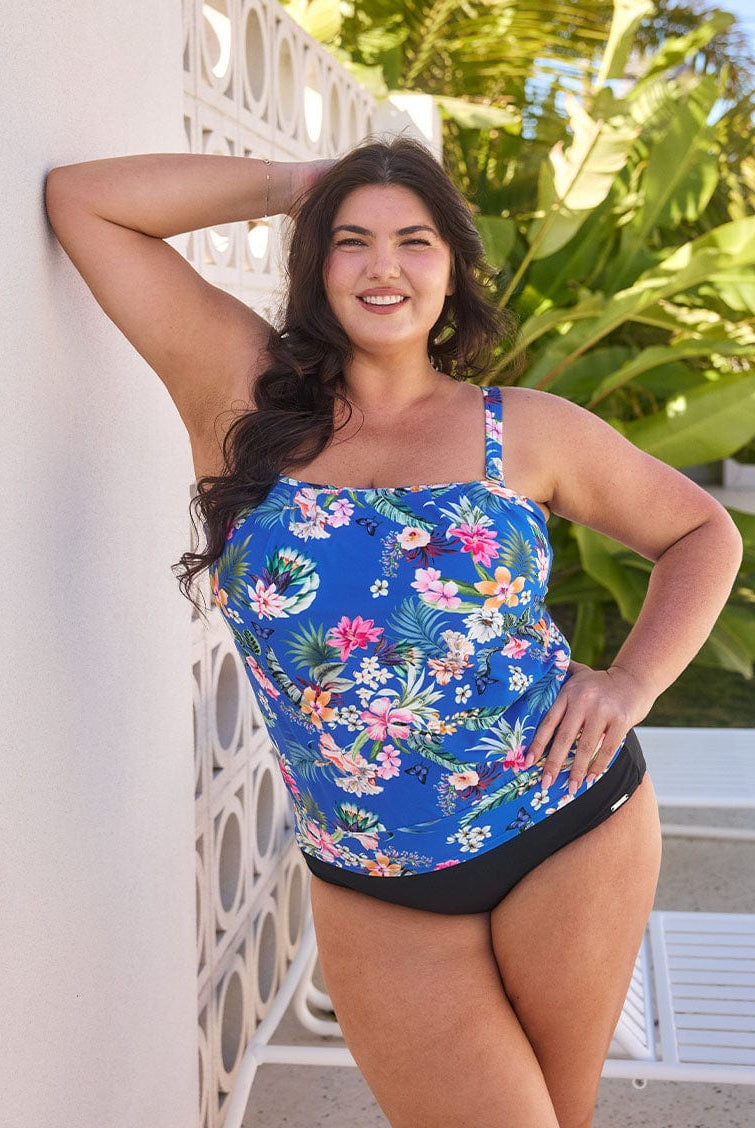 Brunette model wears flattering blue floral bandeau tankini with removable straps and shelf bra