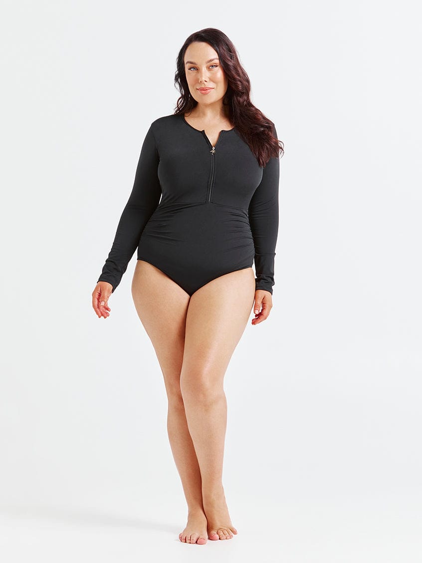 women standing in front of a white wall wearing a black long sleeve one piece swimming suit