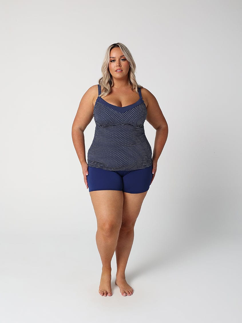 Woman wearing a navy patterned tank top and blue shorts on a white background