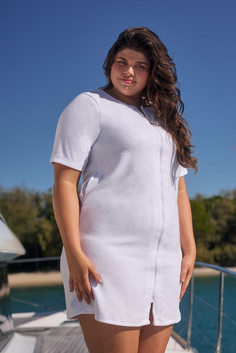 Woman wearing a white dress standing on a boat with a clear blue sky and water in the background