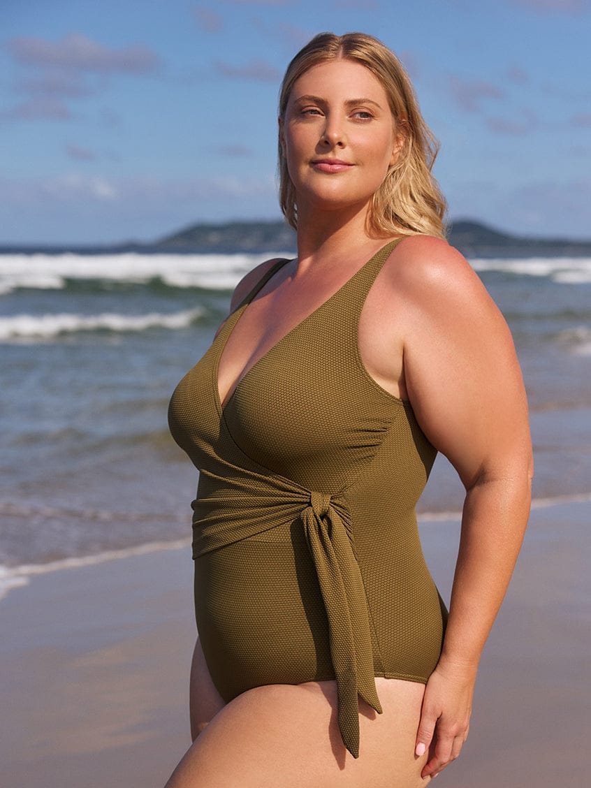 Woman wearing a green swimsuit on a beach with ocean and sky in the background