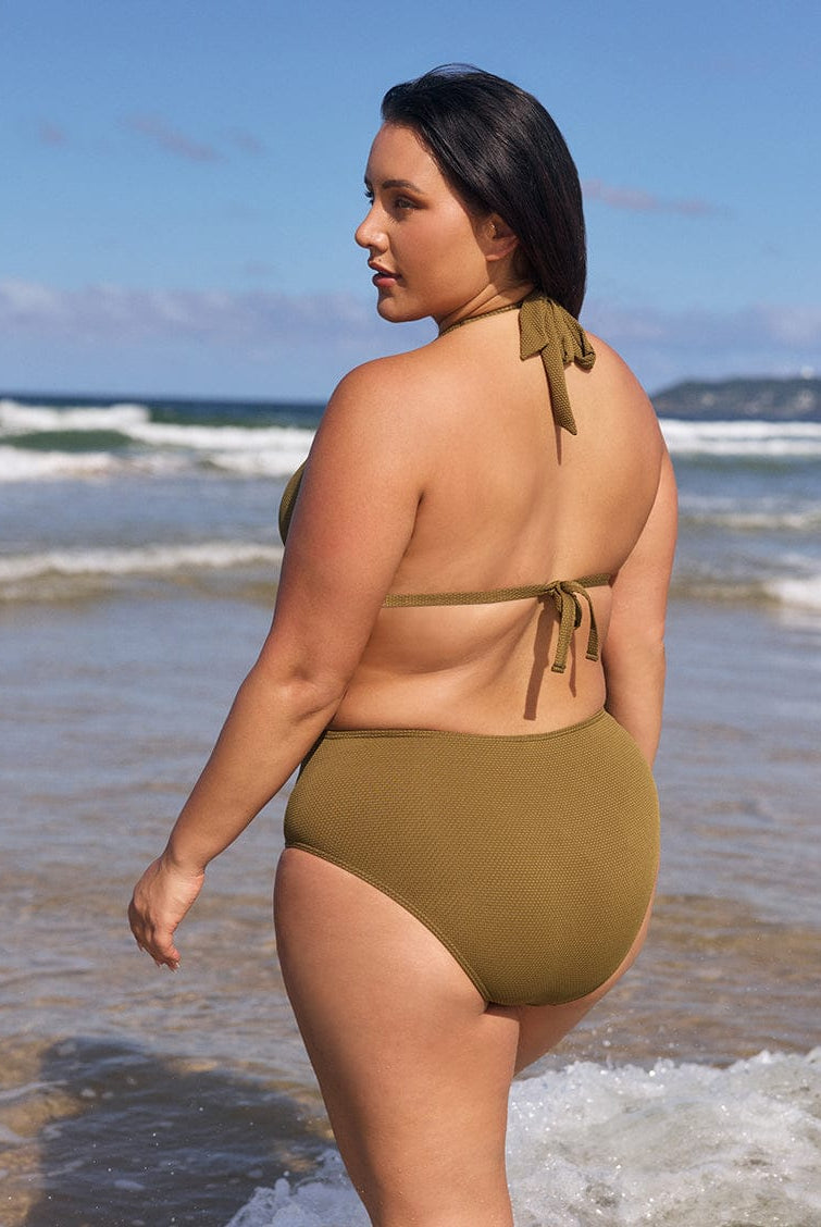 Woman in a green bikini standing on a beach with ocean waves in the background