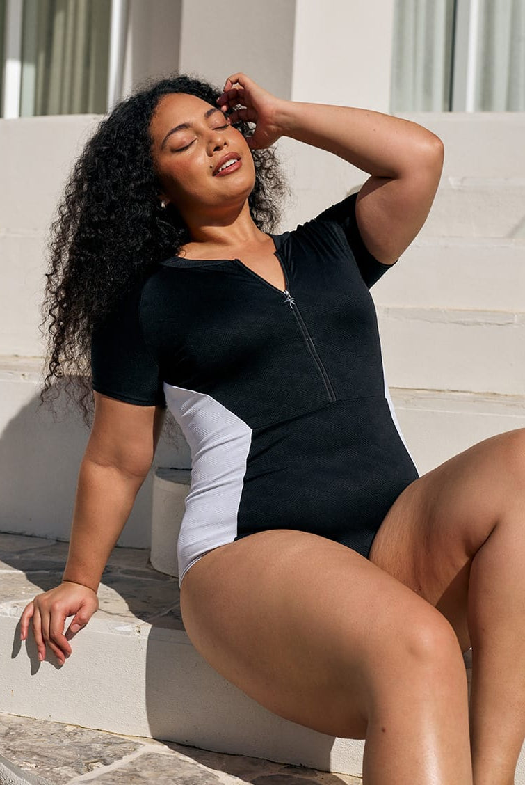 Close up image of model wearing a zip front detail one piece in black and white textured print