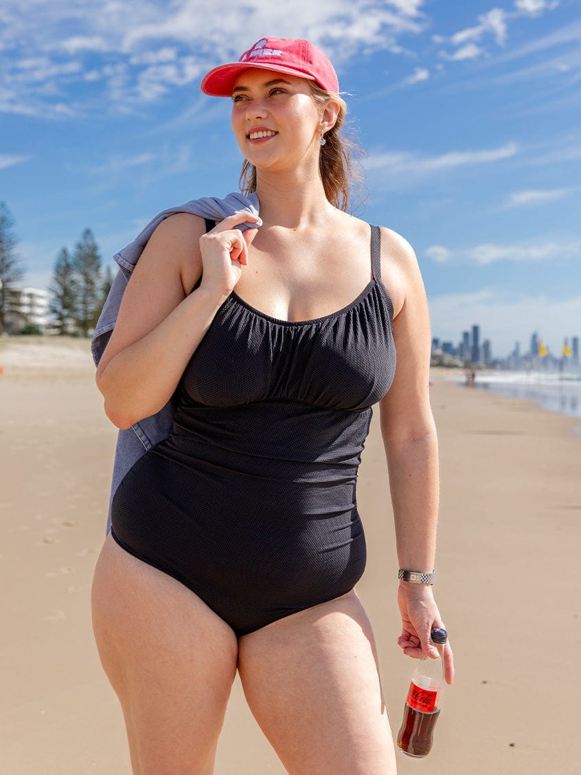 model on beach wearing black textured ruched swimsuit