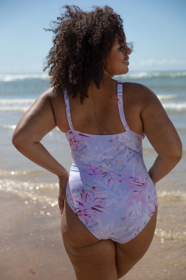 Back of brunette model wearing purple and pink floral one piece with adjustable straps