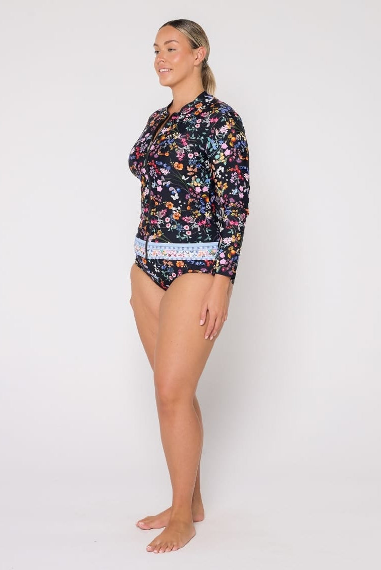 A woman modeling a long-sleeve floral swim top and matching bikini bottoms against a plain light gray studio background.