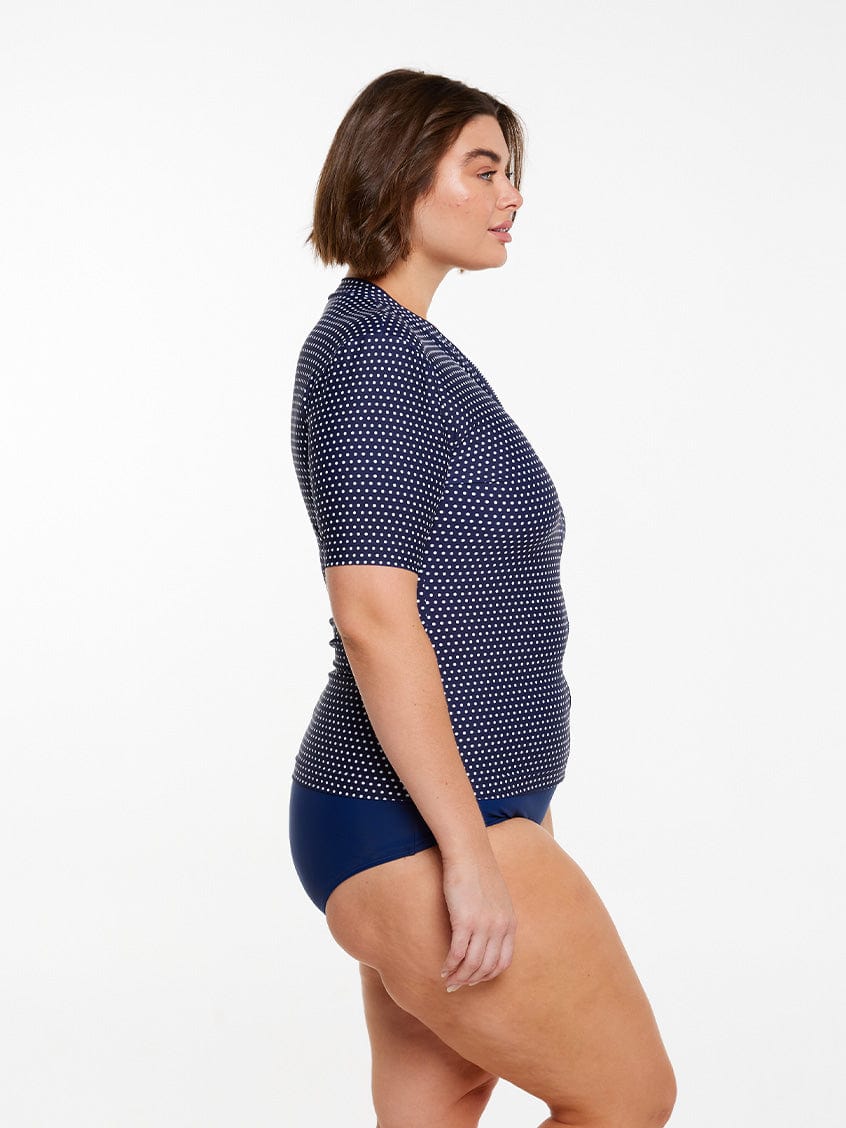model showing side of navy polka dot short sleeve rash vest